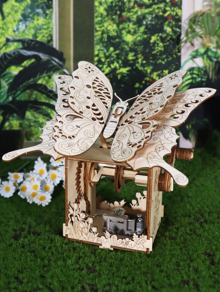 Boîte à musique papillon en bois posée dans l'herbe, devant des fleurs