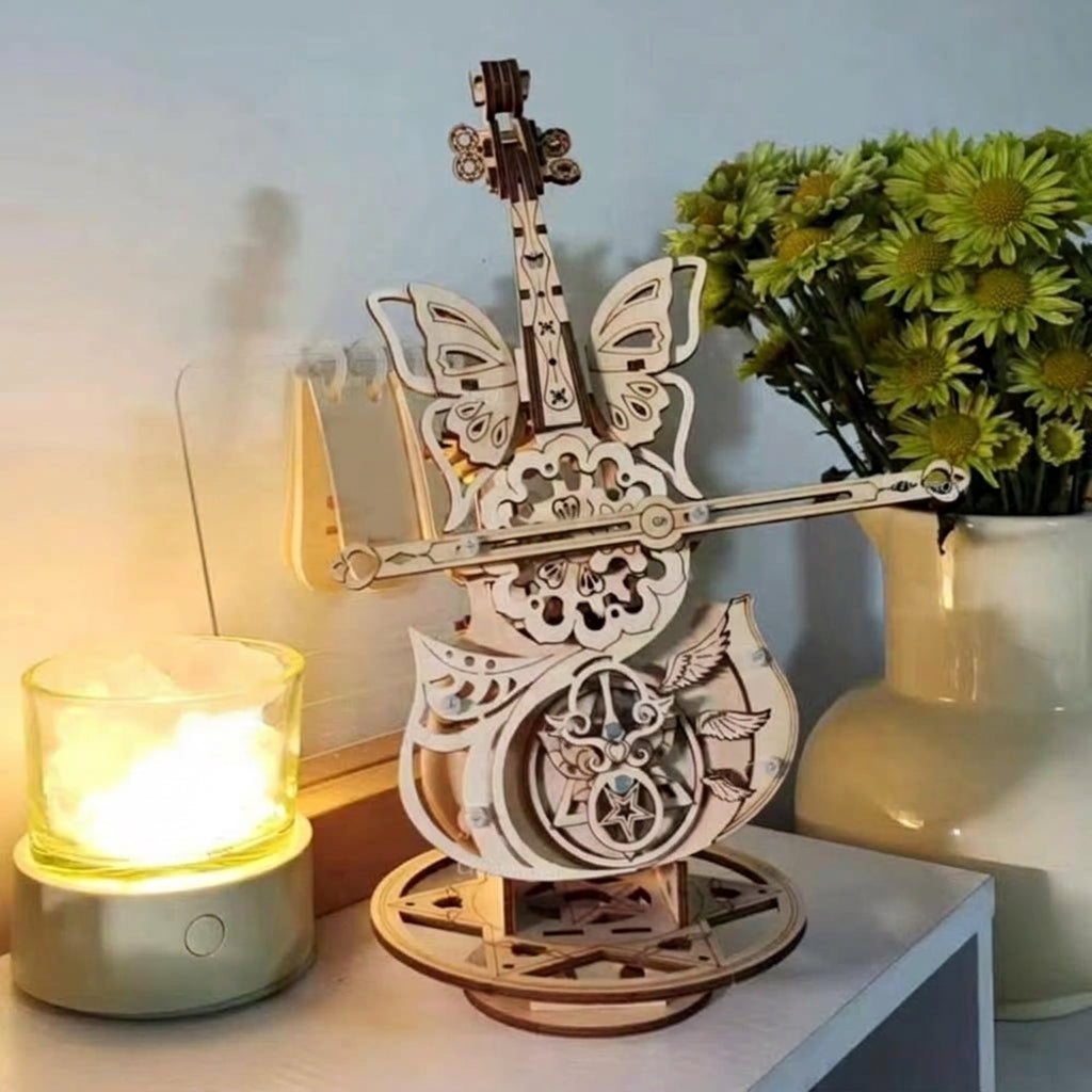 Boîte à musique violoncelle en bois sur une commode, à côté d'une lampe et de fleurs