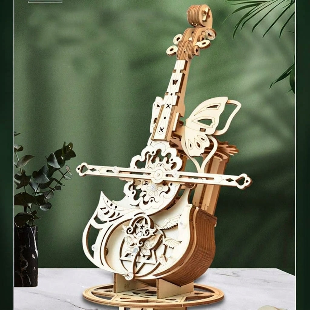Boîte à musique violoncelle en bois devant un fond de plantes vertes