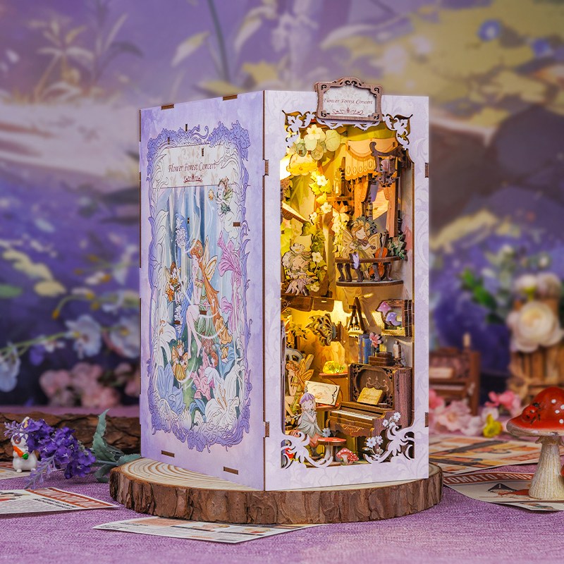 Book nook concert des fées éclairé, posé sur un rondin de bois parmi les fleurs