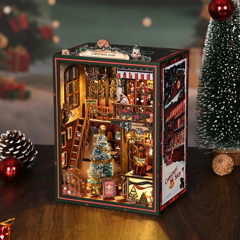 Book nook Noël boutique de cadeaux posé parmi des pommes de pin et des boules
